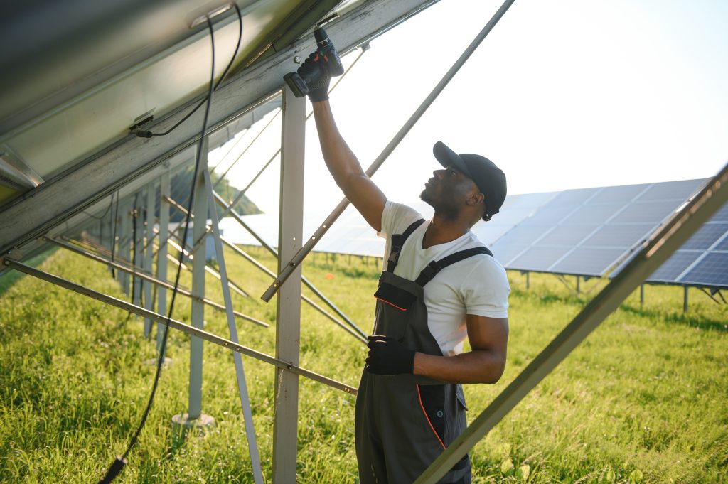 Portrait of african american electrician engineer in safety helmet and uniform installing solar panels.